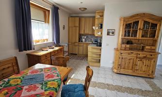 A cozy kitchen with wooden furniture and a dining table. The windows let in a lot of light, and the decor looks inviting.