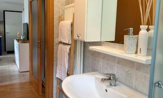 A modern bathroom with a sink and a large mirror. In the background, wooden elements and an open door can be seen.