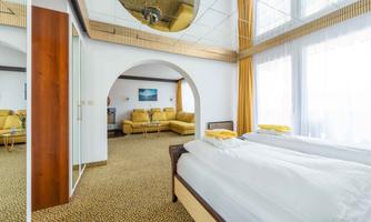 A modern hotel room with a comfortable bed and a cozy living area. Large windows provide plenty of daylight and an inviting atmosphere.