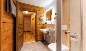 A modern bathroom with wooden paneling and a bright interior. It features a sink, a toilet, and a shower cubicle.