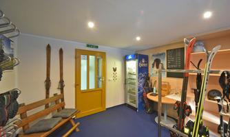 A cozy room with ski equipment and a nice wooden bench. Skis hang on the wall, and there is a refrigerator as well as a reception desk.