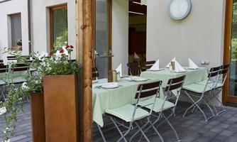 A cozy outdoor area with a covered table and chairs. The tablecloth is green and flower plants are decoratively arranged.
