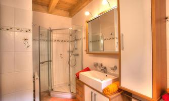 A modern bathroom with a shower cabin and a sink. It has bright walls and wooden ceilings, as well as stylish furniture.