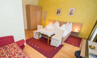 A bright room with a double bed and two chairs at the table. The walls are painted yellow, and there are some pictures in modern frames.