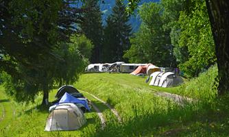 A beautiful campsite with several tents on a green meadow. In the background, trees and caravans are visible.
