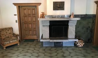 A cozy room with a fireplace and an upholstered armchair. The walls are decorated with green tiles and the floor has an interesting pattern.