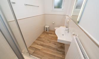 A modern bathroom with a shower and sink. The floor is made of wood and the walls are designed in light colors.