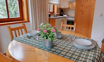 A cozy dining area with a round wooden table and four chairs. On the table is a blooming plant and the dishes are beautifully set.