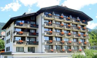 A large hotel building with several balconies and colorful flowers. The sky is clear and the surroundings look calm and inviting.