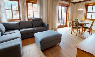 A cozy living room with a gray sofa and a coffee table. There are chairs at the table and plenty of daylight is coming through the windows.