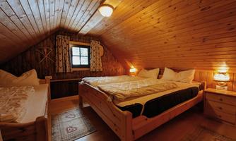 A cozy bedroom with a wooden ceiling, two beds, and a window. The warm lights create an inviting atmosphere.