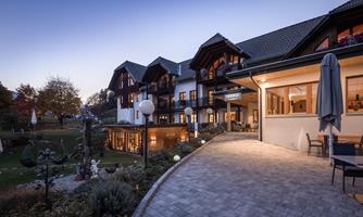 A charming hotel building with a wooden facade at dusk. The well-maintained garden and terrace invite you to relax.