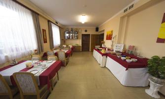 A dining room with several tables and red tablecloths. On one table, there is a buffet with various foods and drinks.
