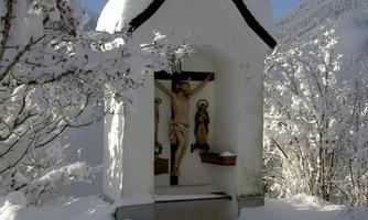 A small chapel in a snowy landscape. The snow covers the surroundings and the trees are frosted.