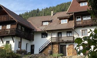 A traditional house in the greenery with stacks of wood and a beautiful garden. The surrounding hills are wooded, creating a tranquil atmosphere.