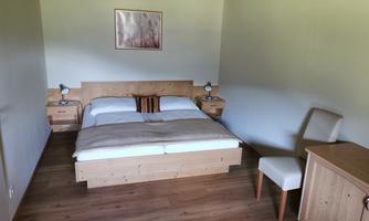 A cozy bedroom with a double bed and wooden furniture. The walls are light-colored and the floor is made of wood, creating a warm atmosphere.