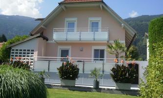 A beautiful house with a red gabled roof and a balcony. The garden is well-maintained and has colorful plants.