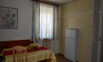 A bright kitchen with a table, chairs, and a refrigerator. The walls are painted in neutral colors, and there are curtains with colorful stripes.