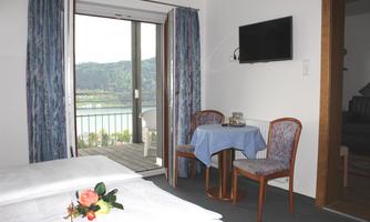 A cozy room with a view of the countryside. There is a small table with two chairs and a TV on the wall.