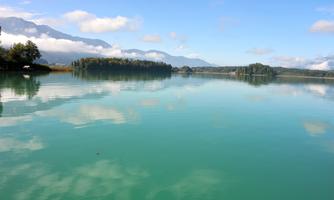 A tranquil lake with clear, blue-green water. In the background, gentle hills and wooded shores are visible.