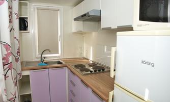 A modern kitchen with purple cabinets and a wood countertop. It includes a stove, a sink, and a refrigerator.