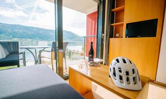 A modern room with a view of the mountains and a balcony. On the table are a bicycle helmet and a bottle, inviting relaxation.