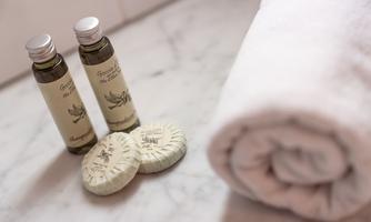 Two bottles of high-quality oil and two soaps lie next to a rolled towel. The scene conveys a sense of relaxation and wellness.