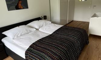 A cozy bedroom with a double bed and a colorful blanket. The room has a wooden floor and a wardrobe.
