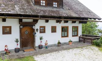 A traditional house with a wooden roof and white walls. In the foreground are plants and small figures.