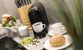 A modern coffee machine is on a kitchen counter. Next to the machine are cups, grapes, and a roll.