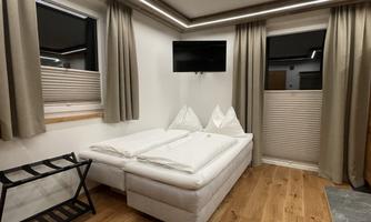 A cozy room with a double bed, a television, and elegant curtains. The wooden floor and the windows with blinds create an inviting atmosphere.