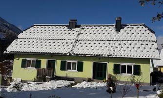A charming green house with a snow-covered roof. The garden and surroundings are also decorated for winter.