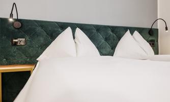A modern bedroom with an elegant, upholstered headboard in green. The white pillows and the duvet create an inviting look.