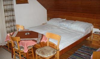 A cozy room with a double bed and a dining table. Wooden panelled walls and carpets give the space a warm atmosphere.