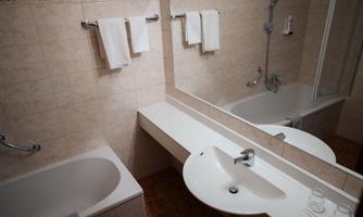 A modern bathroom with a bathtub, a sink, and a large mirror. Towels hang on the wall and the floor is tiled.