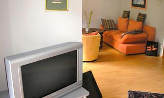 A cozy living room with a television and modern furniture. The orange couch invites you to relax.