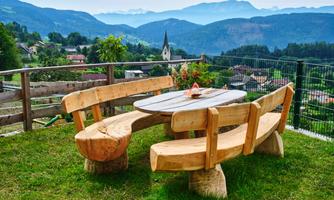 A rustic wooden table with benches in a green setting. In the background, mountains and a small village can be seen.