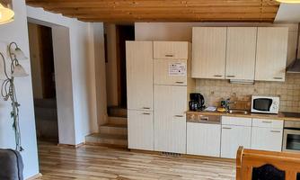 A bright and modern kitchen with wooden shelves and a wooden floor. In the background, stairs are visible that lead to another room.