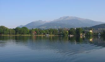 A quiet lake with gentle waves, surrounded by green trees. In the background, majestic mountains can be seen under a clear sky.