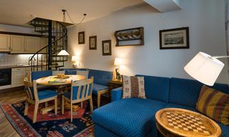 A cozy living room with blue sofas and a round dining table. The modern kitchen and the spiral staircase give the room an inviting character.