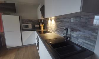 A modern kitchen with white cabinets and a dark countertop. The walls are decorated with gray tiles, and there is a microwave.