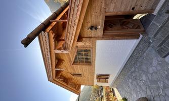 A traditional wooden house with a red roof and an inviting entrance door. Surrounded by a picturesque mountain landscape and clear sky.