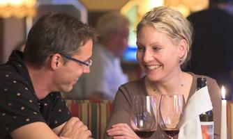 A smiling couple sits in a restaurant and enjoys a conversation. On the table are wine glasses and a candle that creates a cozy atmosphere.