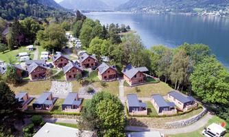 A variety of log cabins is situated picturesque by the shore of a lake. Surrounded by trees and green meadows, the landscape offers a calm and relaxed atmosphere.