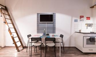 A modern dining room with a table, six chairs, and a television on the wall. On the left, a wooden ladder leads to an upper floor.