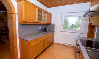 A modern kitchen with wooden cabinets and a large window. The floor is wooden, and the countertop is gray.