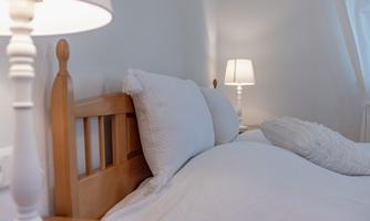 A cozy bedroom with a wooden bed and white pillows.  
Next to the bed are two elegant lamps that provide a warm light.