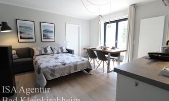 A bright and modern living kitchen with a sofa bed and a dining table. Large windows provide plenty of daylight.