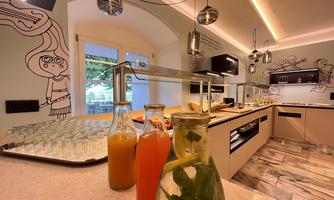 A modern kitchen with a buffet and various drinks in glass carafes.  
Walls are decorated with creative drawings and the lighting is designed to be pleasant.