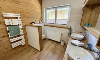 A modern bathroom with wood paneling and two sinks. The large windows provide plenty of daylight.